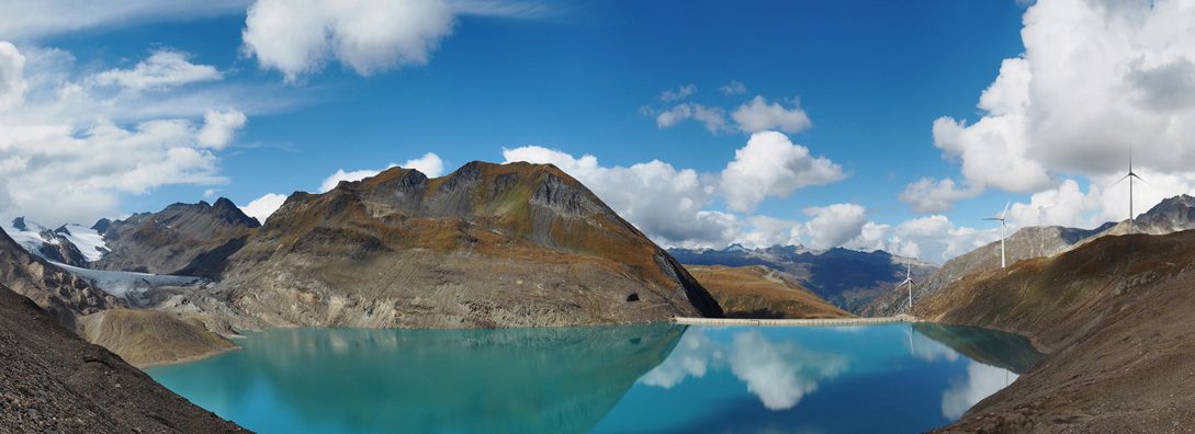 Large size panorama view of Griessee (Gries Lake) and Griesgletscher (Gries Glacier) just across the border between Canton of Ticino and Canton Valais in Switzerland and the international border between Italy and Switzerland in the Lepontine Alps. Near Bedretto Valley and Nufenen mountain pass on the Swiss side and Formazza Valley in Piedmont on the Italian side. Four Wind Turbines visible in the distance on Nufenen mountain pass.