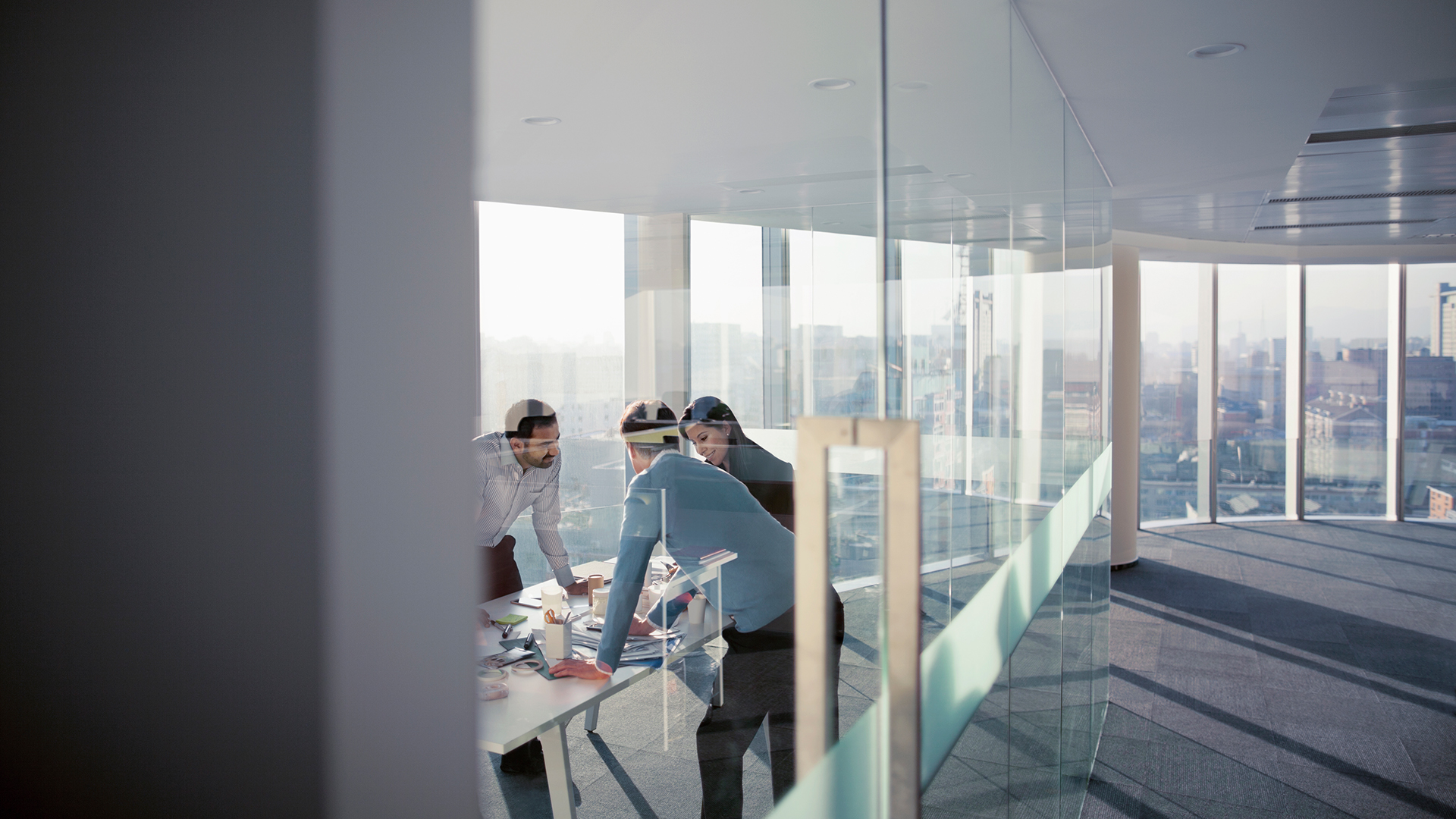 Group of diverse multi-ethnic Hispanic Middle Eastern Caucasian business people designers planners engineers architects consultants in contemporary modern meeting conference table room with layouts designs plans to review make plans in innovation creativity consulting business in studio work room preparation choice critique feedback complexity collaboration teamwork community expertise dusk afternoon ideas brainstorming cooperation cityscape city downtown urban decisions choice