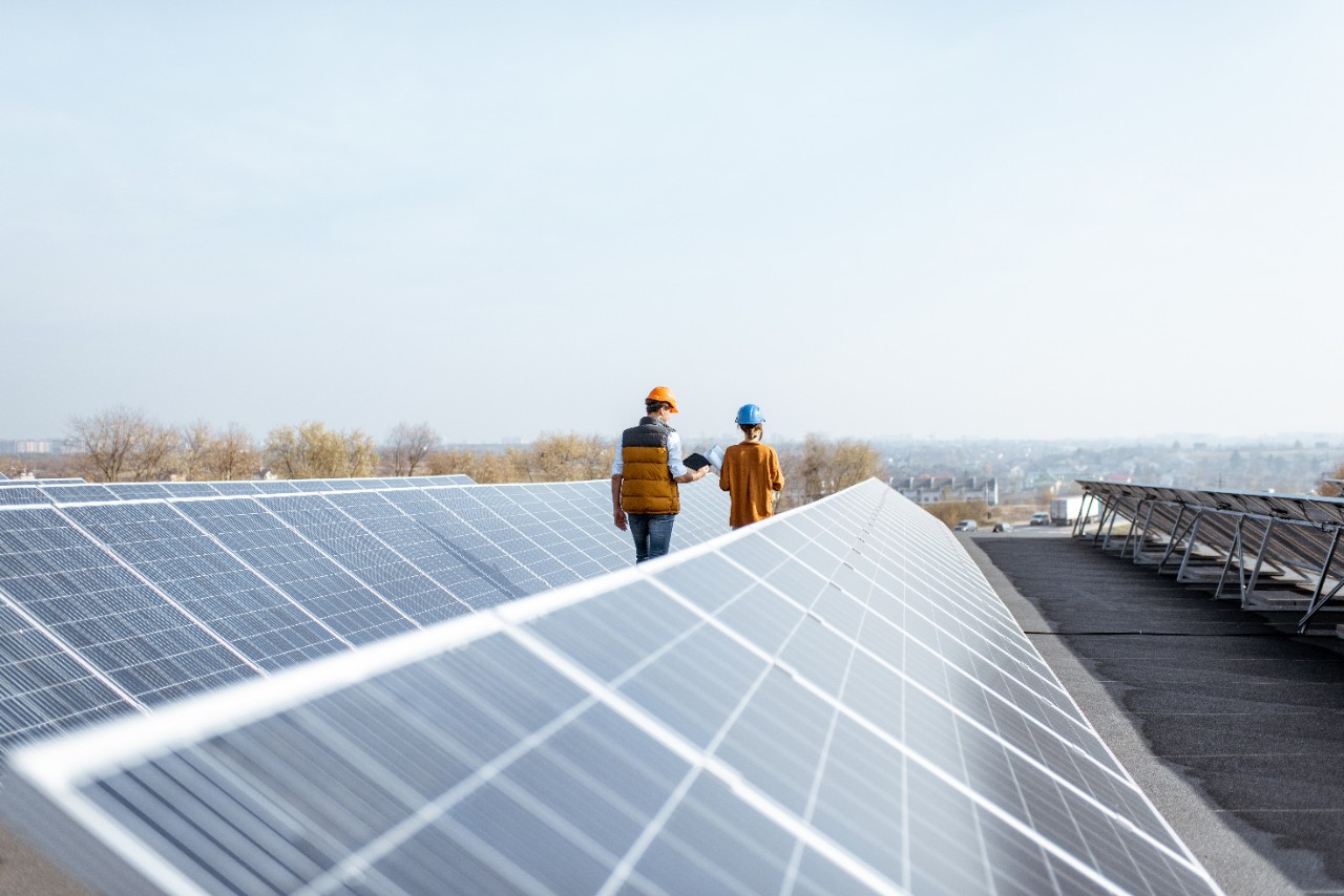 View on the rooftop solar power plant with two engineers walking and examining photovoltaic panels. Concept of alternative energy and its service